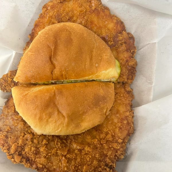 Crispy fried chicken sandwich with pickles on a bun, cut in half, on white paper.