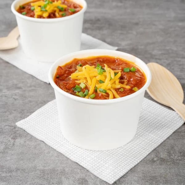 Two cups of Clover Leaf chili topped with shredded cheddar cheese and green onions, with wooden spoons.
