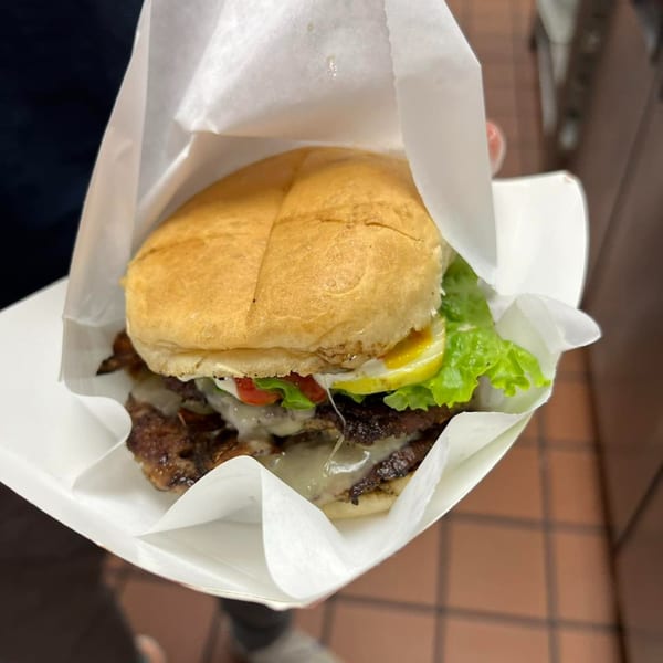 A Clover Leaf on Franklin double cheeseburger with lettuce, tomato, and pickles in a paper wrapper.