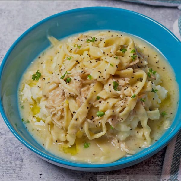 A blue bowl filled with creamy chicken and noodles over mashed potatoes, garnished with parsley.