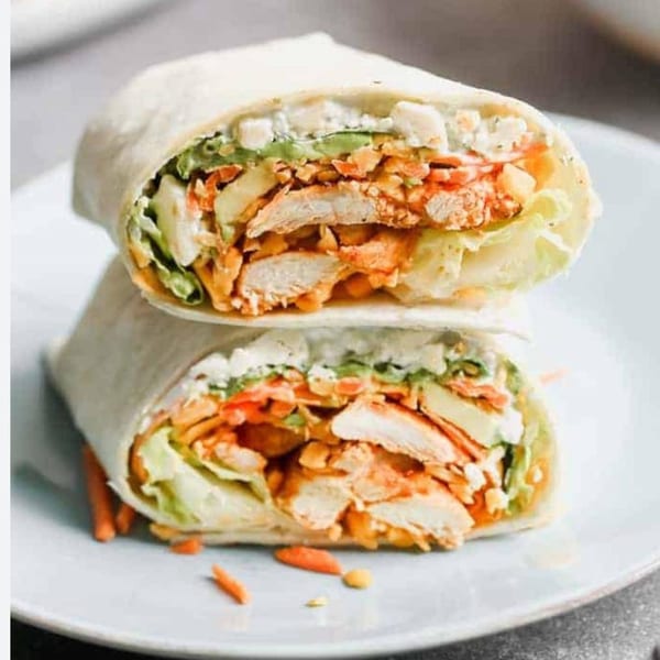 Two halves of a chicken wrap, filled with chicken, lettuce, carrots, and white sauce.